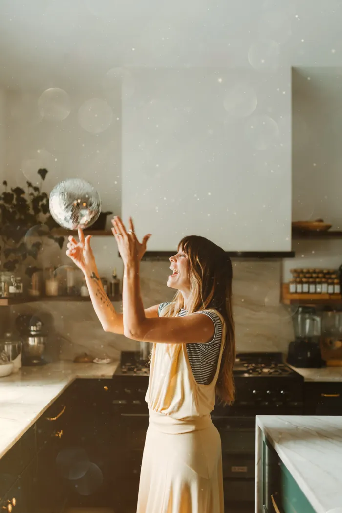 Jess Manuel laughing while balancing a disco ball on her finger in her kitchen