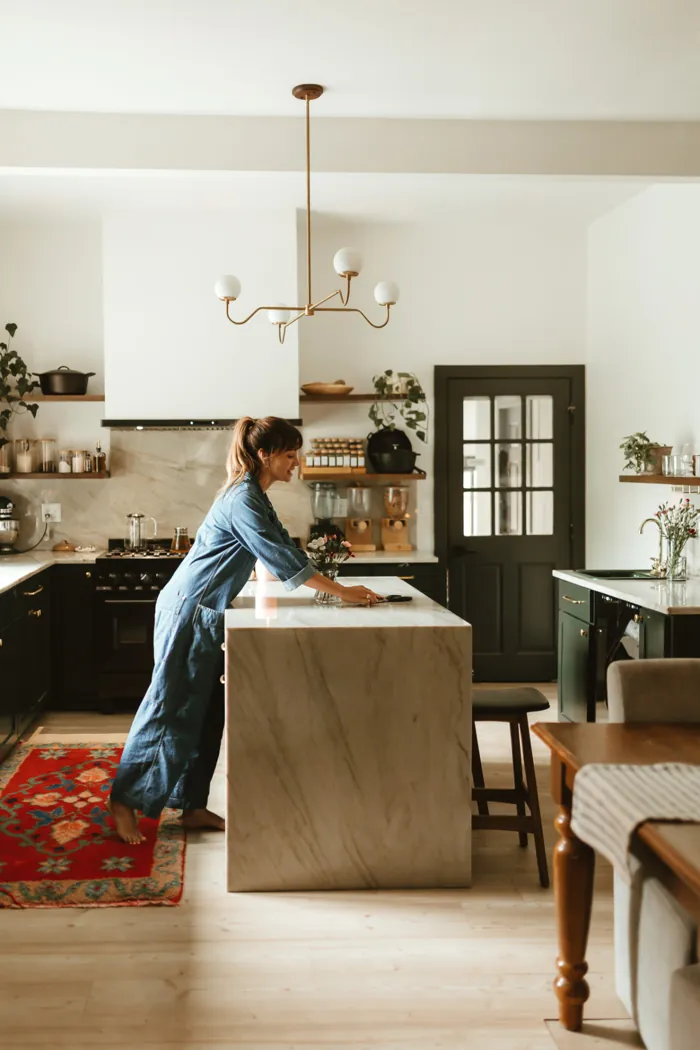 Jess Manuel in a denim jumpsuit leaning on her marble kitchen island