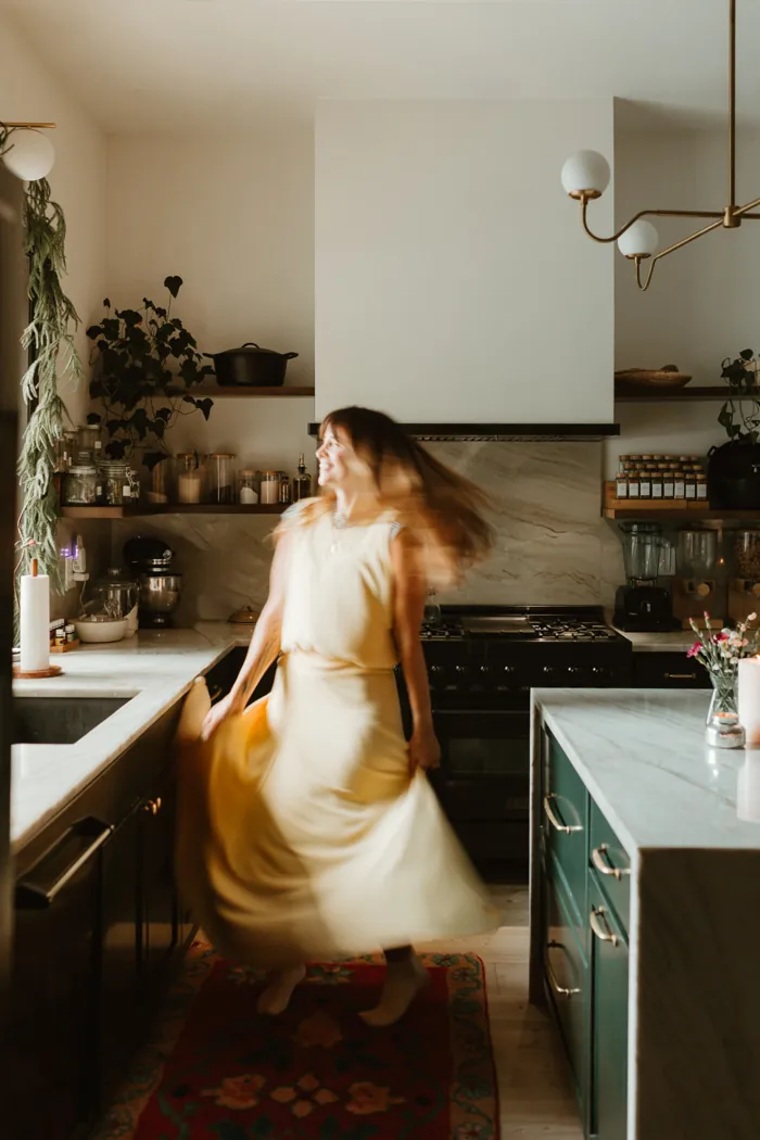 Jess Manuel twirling in a pale yellow dress in her kitchen