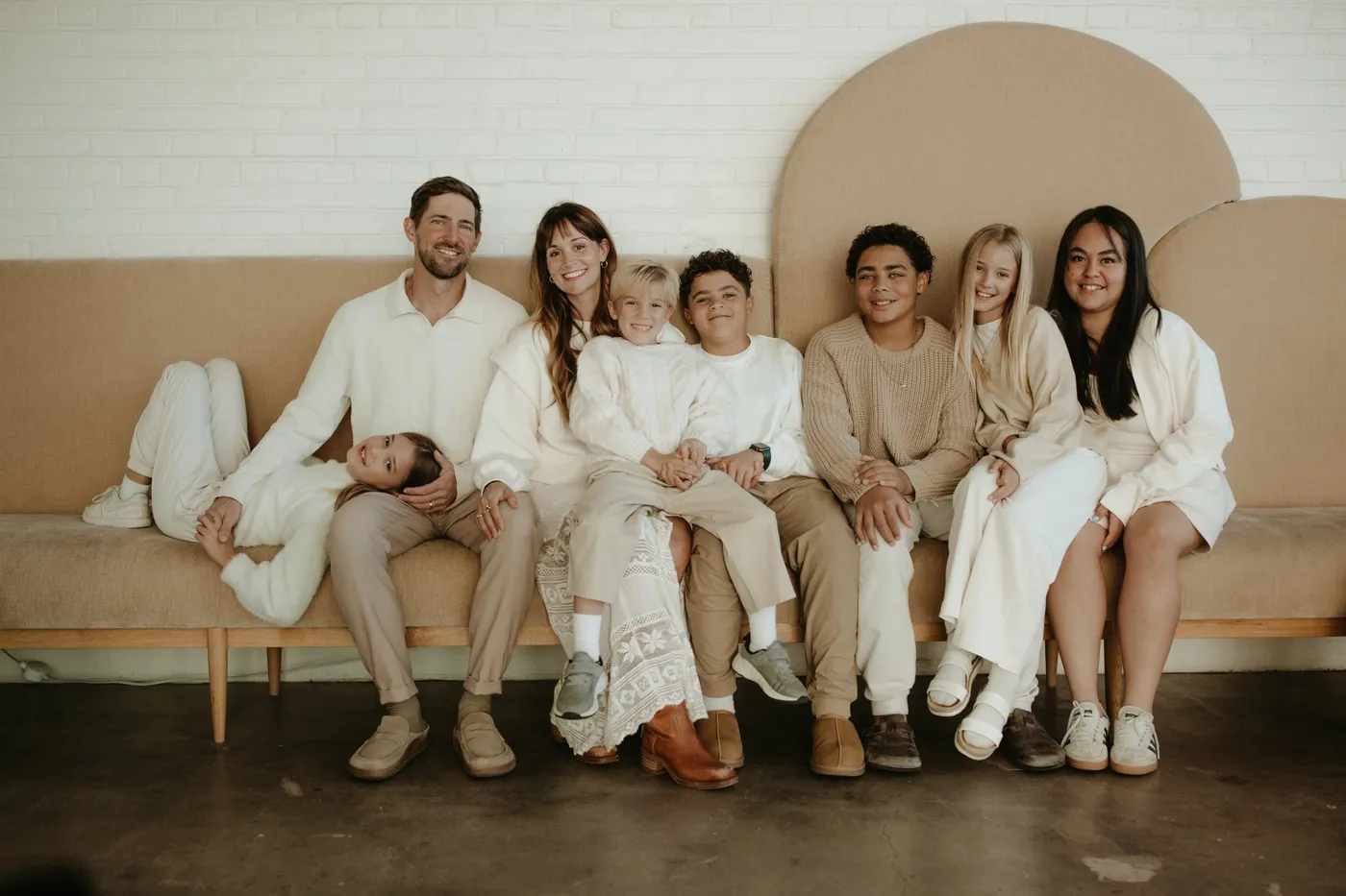 Jess Manuel, Parker, and their six children sitting together on a tan couch