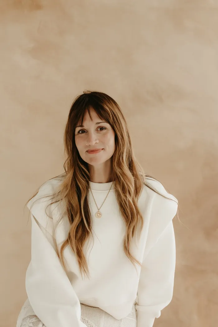 Portrait of Jess Manuel smiling in a cream sweatshirt against a warm plaster wall